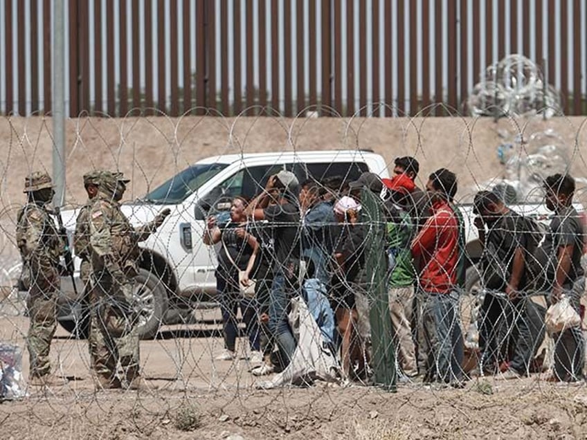 Migrants listen to members of the Texas National Guard after passing through razor wire fr