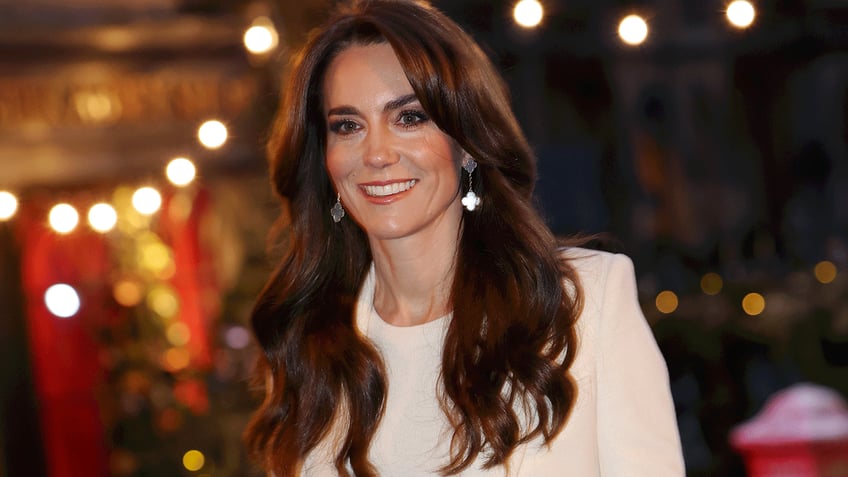 Kate Middleton in a white blazer and shirt smiles as she walks