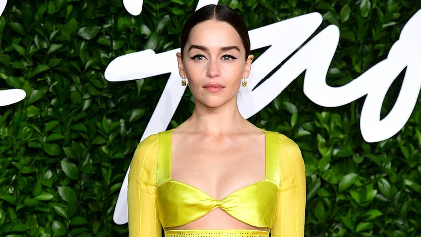 Emilia Clarke in a neon yellow/lime green dress poses seriously on the carpet