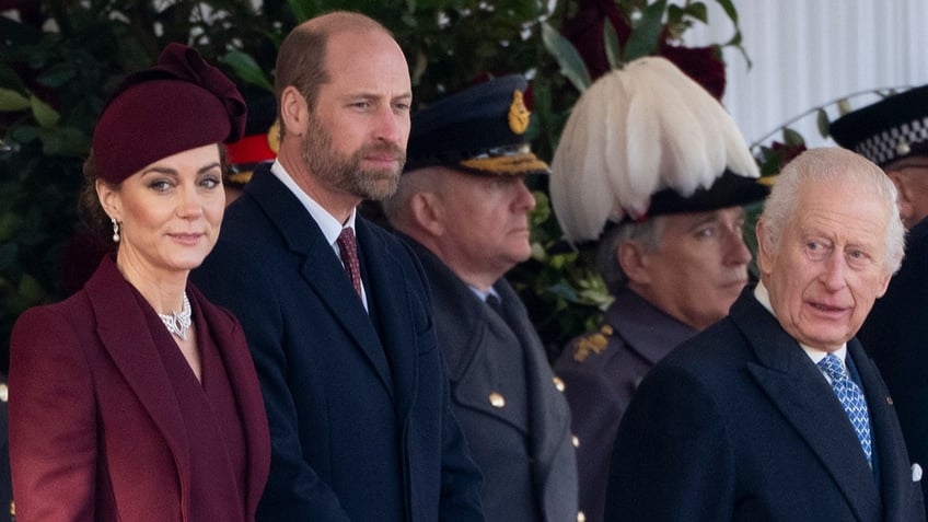 Kate Middleton in a purple coat standing next to Prince William and King Charles as they both wear navy suits.