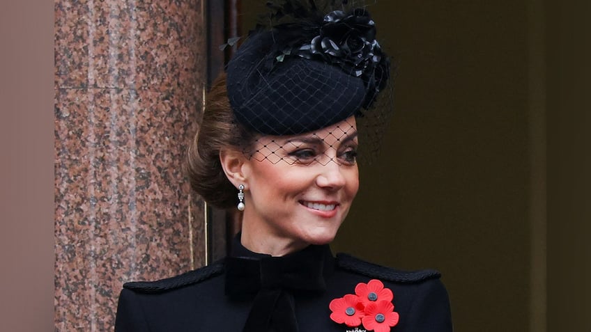 Close up of Kate Middleton smiling wearing black dress and hat and poppy pin