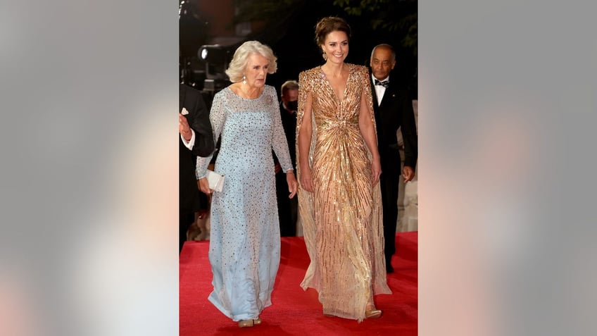 Queen Camilla in a sparkling pale blue dress walking next to Kate Middleton who is wearing a gold sparkling dress.