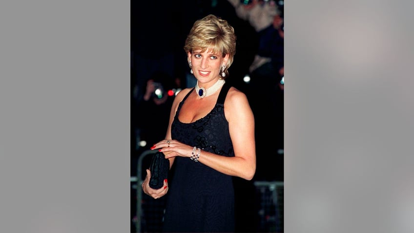 Princess Diana wearing a dark blue strappy dress with a pearl and sapphire choker as she holds a clutch.