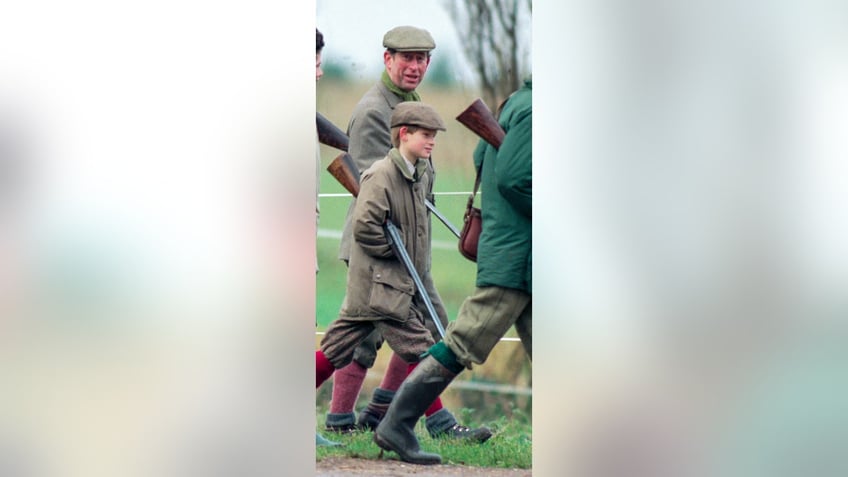 A young Prince Harry holding a gun walking alongside his father.