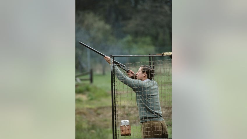 Prince Charles outdoors in a green sweater shooting