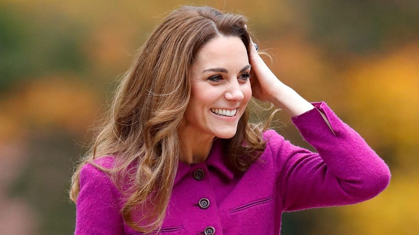Kate Middleton touching her hair in a bright pink coat dress