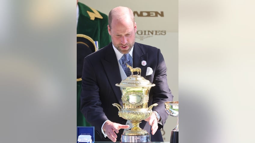Prince William in a dark suit aims to grab trophy.