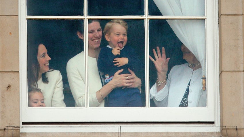 A young Prince George being held by his nanny as they look outdoors.