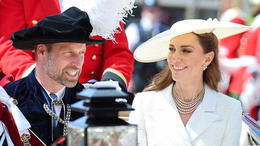 Prince William and Kate Middleton smiling at each other in royal formal wear sitting on a carriage.