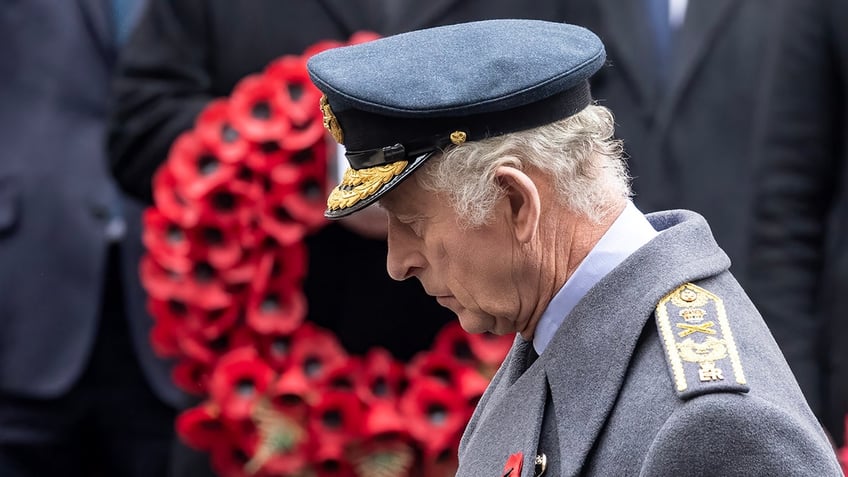 King Charles standing in uniform in front of a wreath of red poppies.