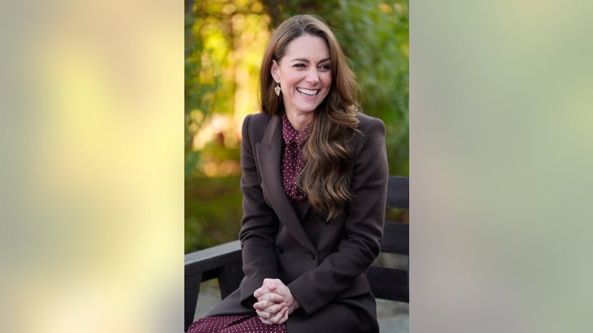 Kate Middleton in a brown suit and smiling.