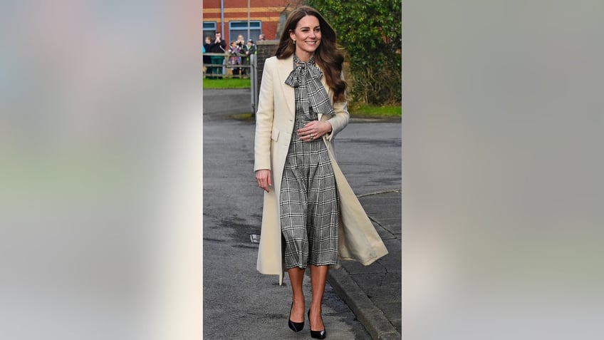 Kate Middleton wearing a plaid black and white dress and an ivory coat.