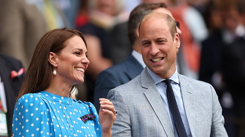 Kate Middleton wearing a light blue polka dot dress smiling next to Prince William