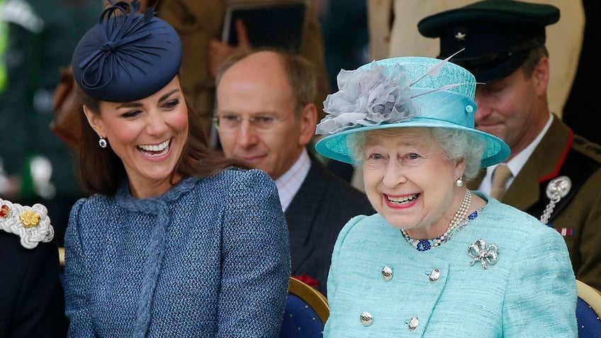 Kate Middleton in a blue suit and matching hat laughs as shes seated next to Queen Elizabeth in a pale turquoise outfit and matching hat