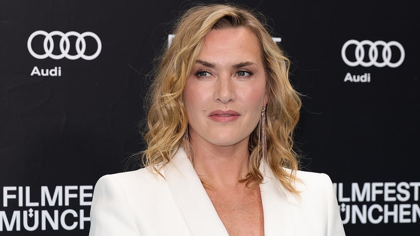 Kate Winslet looks to her right on the carpet wearing a white suit