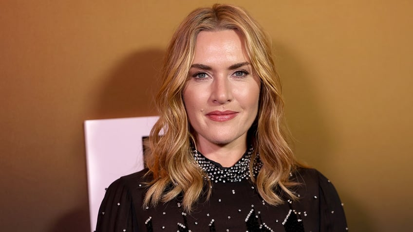 Kate Winslet in a black dress with little embellishments stares at the camera on the carpet