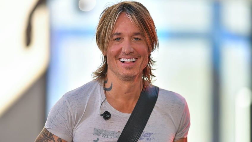 Keith Urban smiles on stage in New York City with a guitar slung across his back