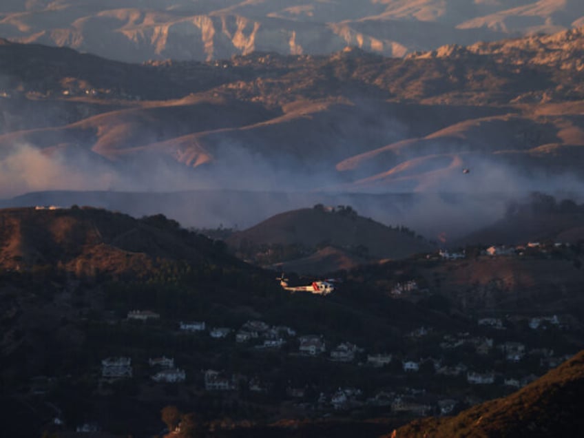 A CalFire helicopter flies near plumes of smoke from the Kenneth Fire in West Hills, Calif