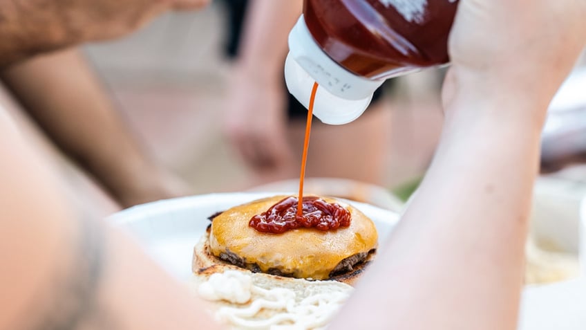 Person squeezes ketchup onto cheeseburger.