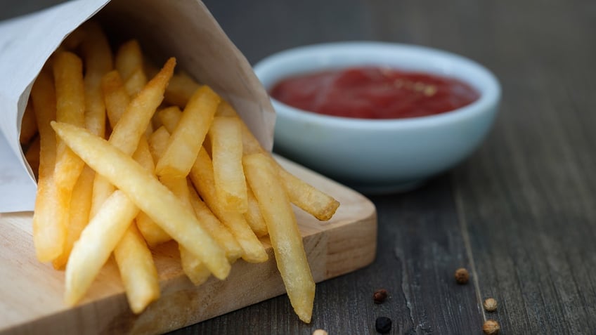 Container of French fries next to bowl of ketchup.