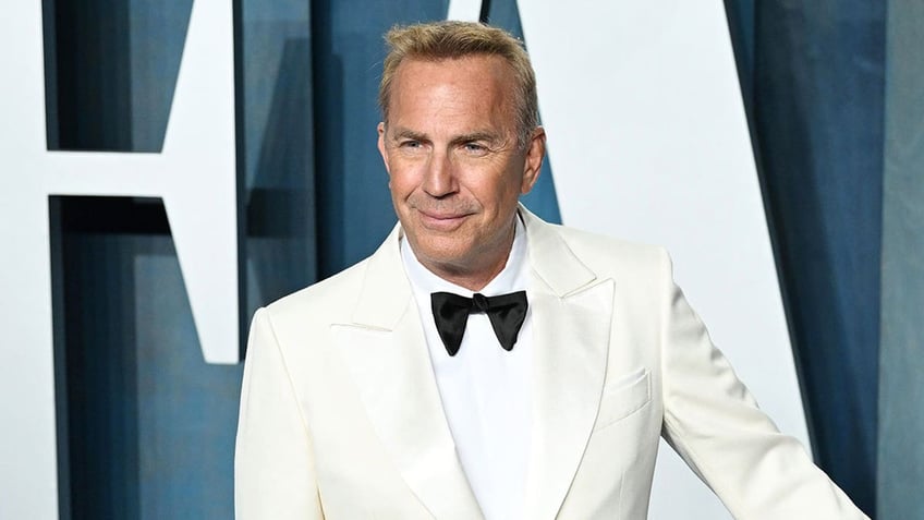 Kevin Costner wears white tuxedo with black bow tie.