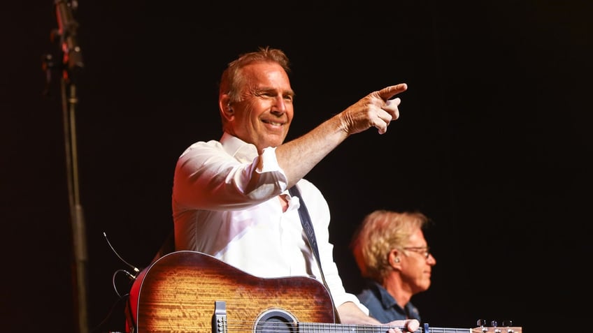 Kevin Costner strums guitar on stage in Nashville