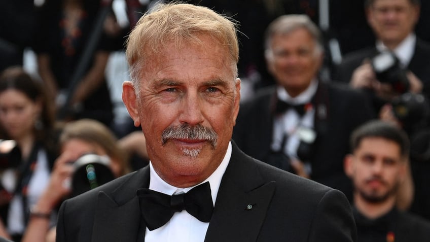 Kevin Costner in a classic tuxedo flashes a slight smirk in Cannes
