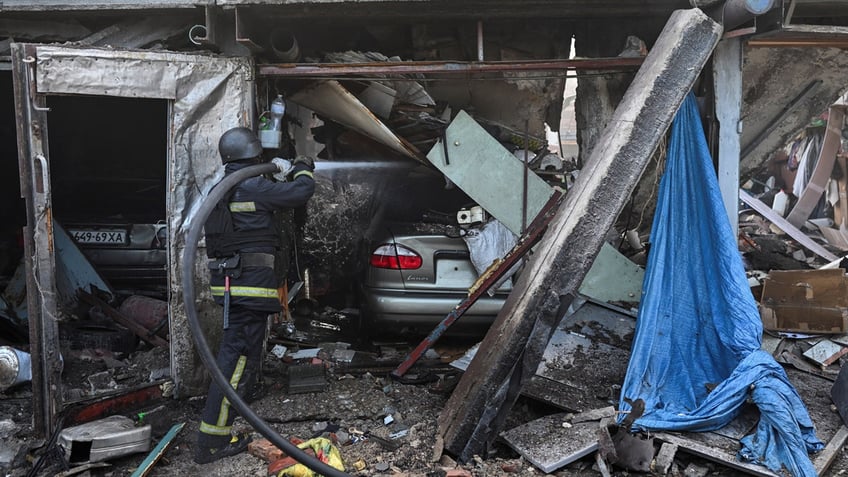 A rescue member works at a site of a Russian air strike. Cars are seen beneath rubble.