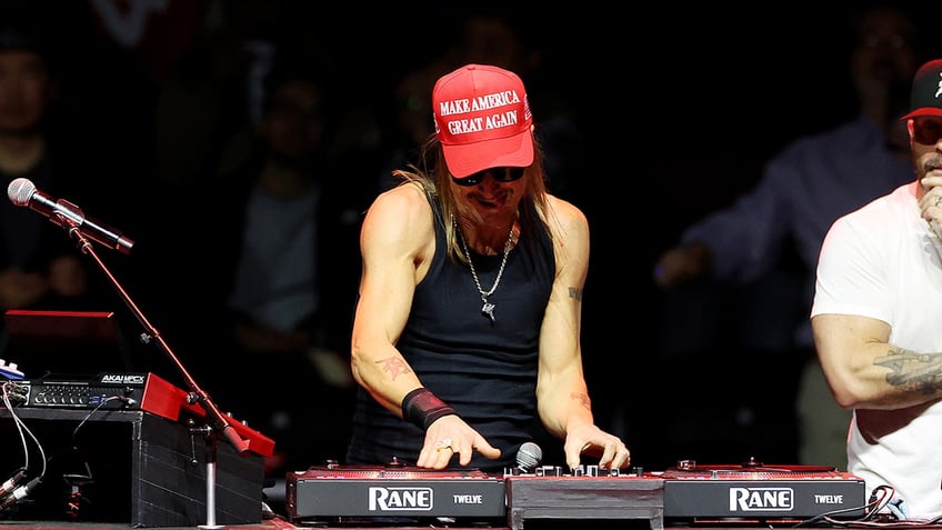 Kid Rock in a black tank top and a red 'Make America Great Again' hat plays with the music board on stage at the MAGA Victory Rally