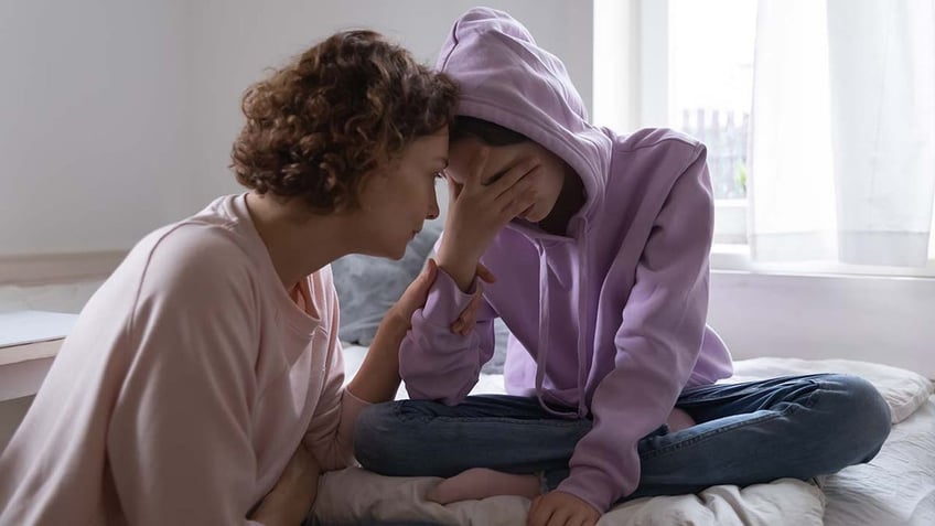 Worried parent comforting depressed crying teen daughter 