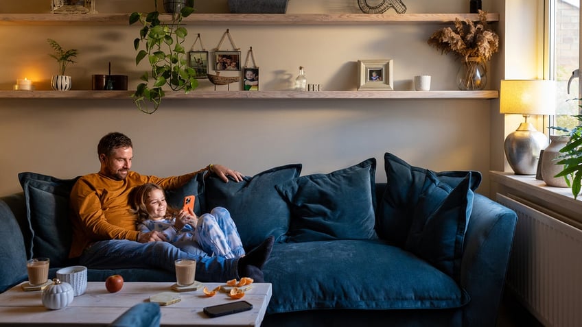 father lying down on the sofa with his daughter on her phone