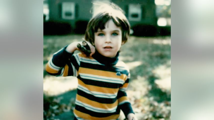 Collier Landry wearing a striped shirt and standing in front of a house.