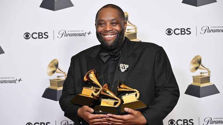 Killer Mike smiles holding his 3 Grammy Awards