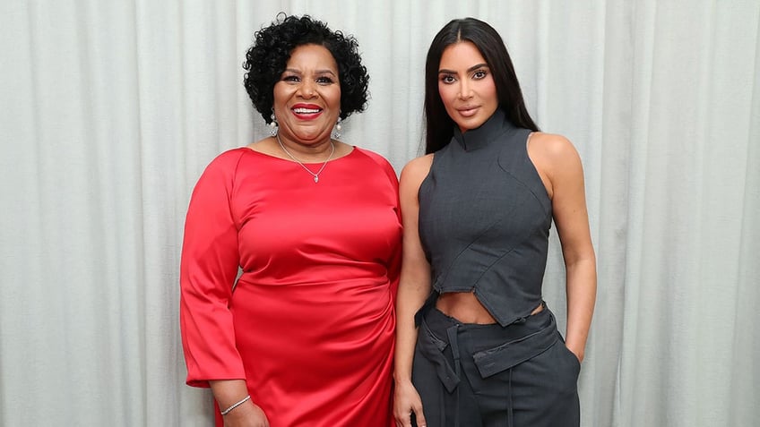 Alice Marie Johnson in a red dress smiles next to Kim Kardashian in a two piece grey set
