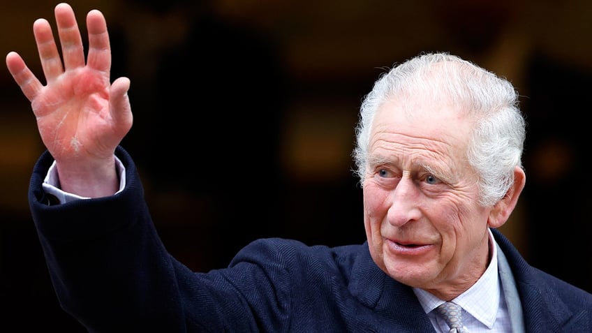 King Charles in a navy suit waves to spectators as he leaves The London Clinic