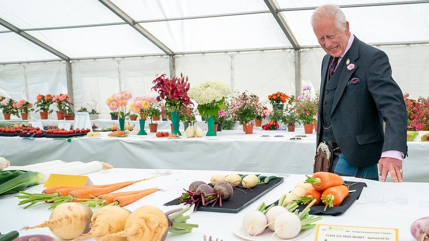 King Charles admiring vegetables laid out on a white table.