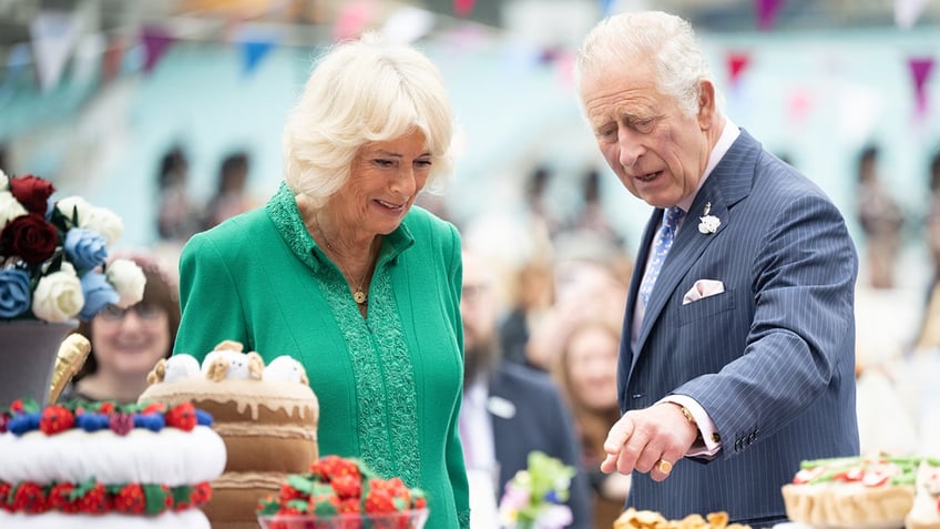 Queen Camilla and King Charles admiring a row of pastries.