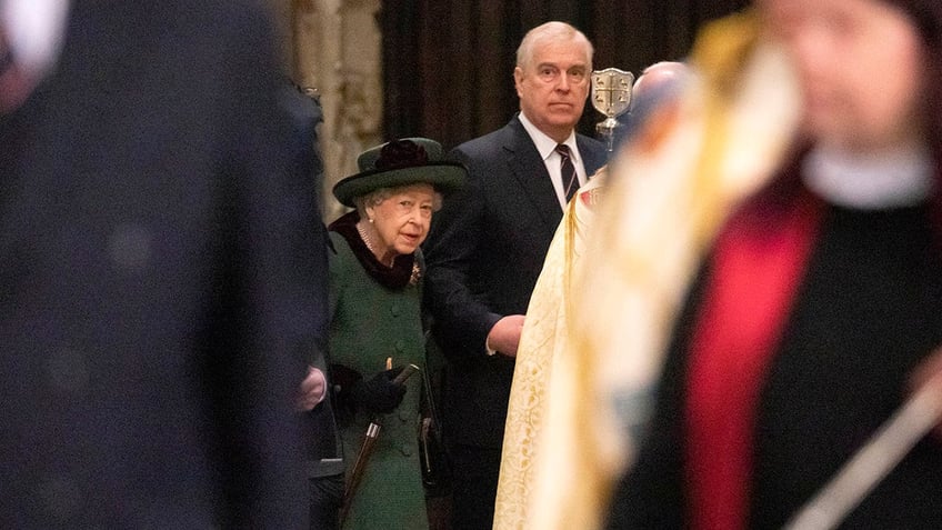 Queen Elizabeth in a green coatdress and matching hat walking alongside Prince Andrew inside a church.