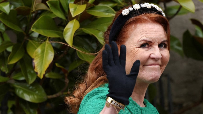 Sarah Ferguson in a green suit and black bejeweled headband waves wearing a black glove