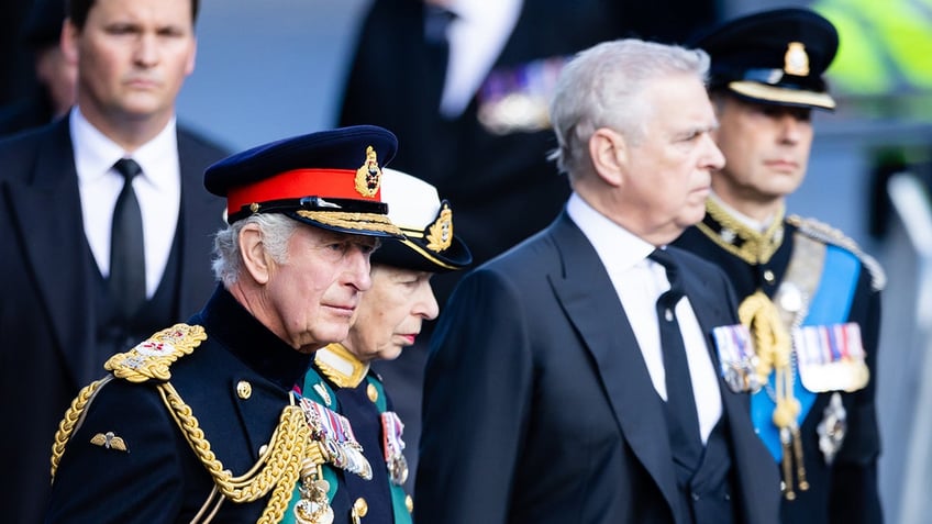 Prince Andrew in a suit looking away from King Charles in military wear.