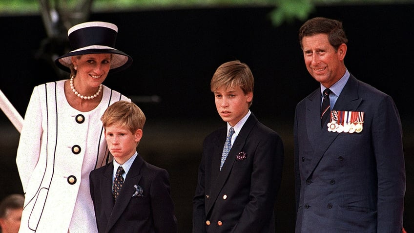 Prince Charles and Princess Diana smiling as they stand next to their two sons Prince Harry and Prince William in matching suits