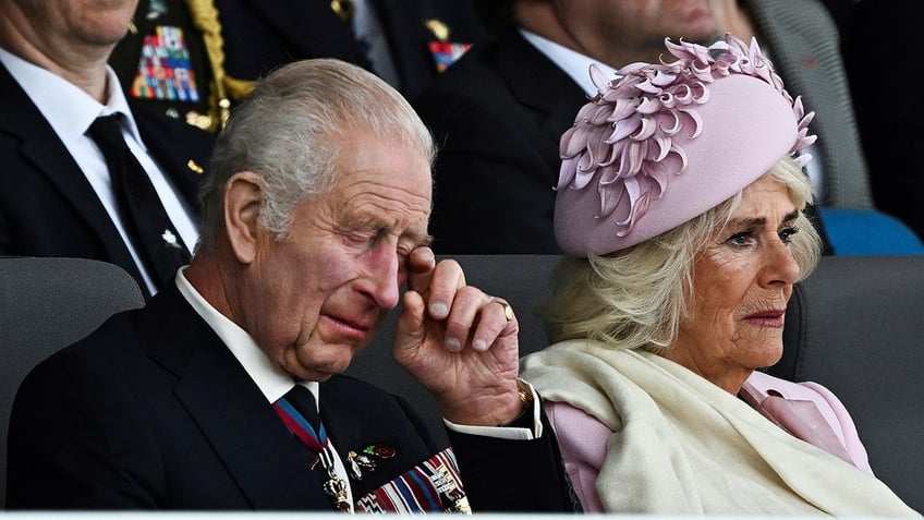 King Charles III wiping away a tear next to Queen Camilla, who is also tearing up