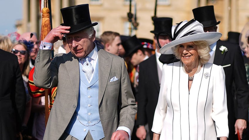 King Charles tipping his top hat next to a smiling Queen Camilla