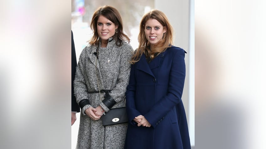 Princess Eugenie wearing a grey coat next to Princess Beatrice in a navy blue coat