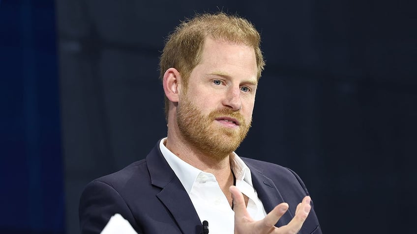 Prince Harry in a navy suit and white shirt in mid conversation.