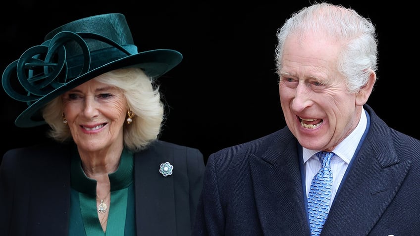 Queen Camilla in a black jacket and queen blouse with a matching green top hat soft smiles as she walks alongside King Charles in a black suit and blue tie looking very jovial