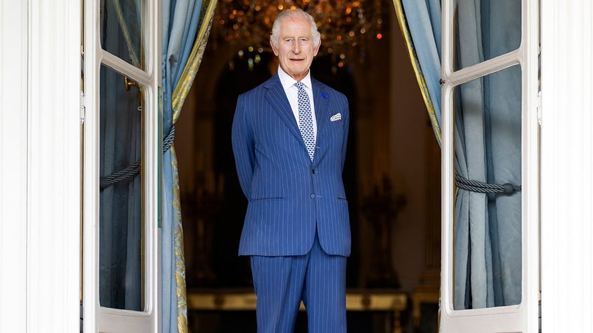King Charles wearing a blue suit standing and looking serious