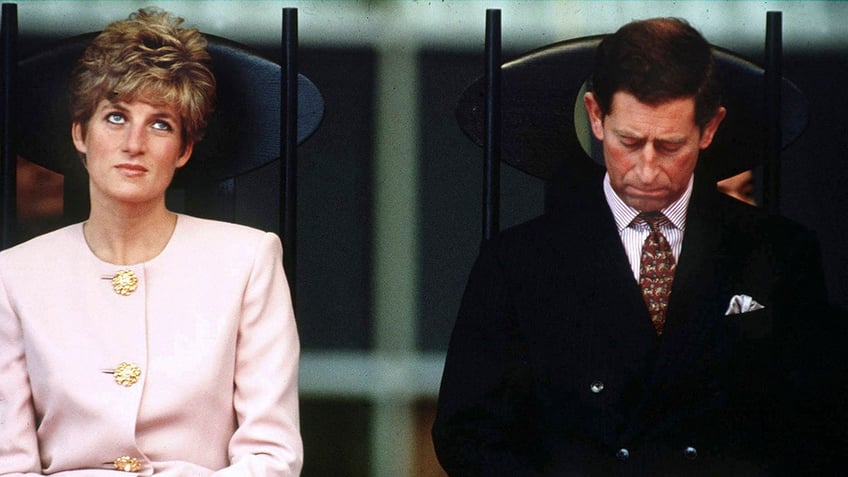 Princess Diana wearing a pink blazer sitting next to King Charles in a dark suit.