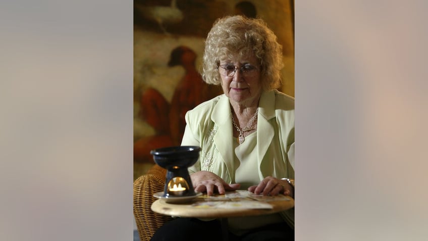 Betty Palko wearing a yellow suit looking at a deck of tarot cards.