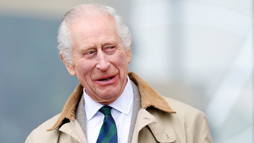 A close-up of King Charles in a trench coat smiling